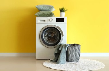 Sarı duvarın yanında battaniye ve çamaşır makinesi olan hasır sepet.