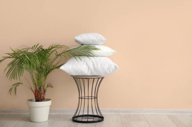 Beyaz yastıklı masa ve bej duvarlı ev bitkisi.