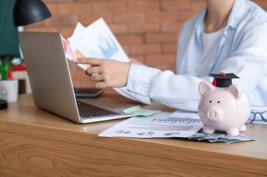 Ahşap masada dizüstü bilgisayarla mali durumunu hesaplayan bir kız öğrenci. Öğrenci kredisi kavramı