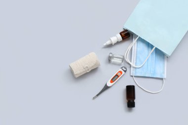 Tıbbi maskeli alışveriş çantası, elastik bandaj ve gri arka planda termometre.