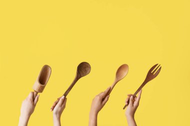 Sarı arka planda ahşap mutfak aletleri olan kadın eller.