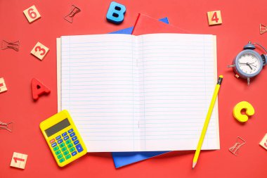 Farklı okul kırtasiyesi ve kırmızı arkaplanda boş defter