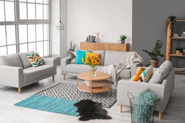 Işıl ışıl oturma odasının içinde güzel ayçiçekleri olan rahat gri kanepeler ve vazolar.