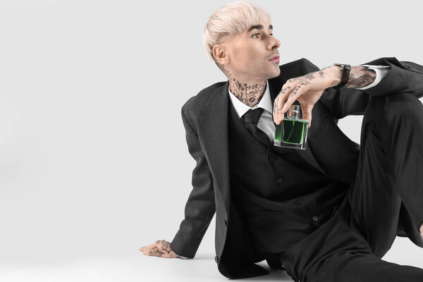 Татуированный молодой человек в костюме с духами сидя на светлом фоне