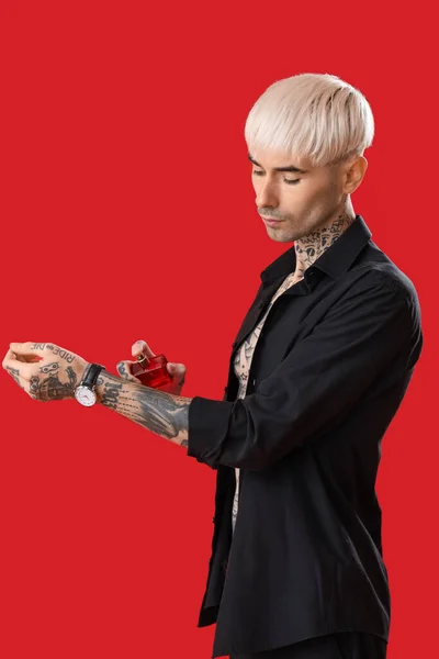 Hombre Joven Tatuado Rociando Perfume Sobre Fondo Rojo — Foto de Stock