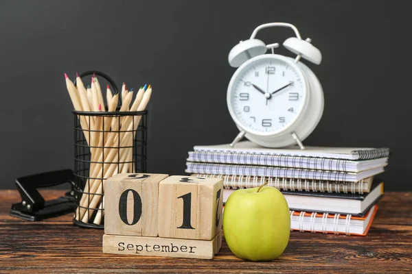 Different stationery, alarm clock and calendar with date SEPTEMBER 1 on wooden table against black chalkboard