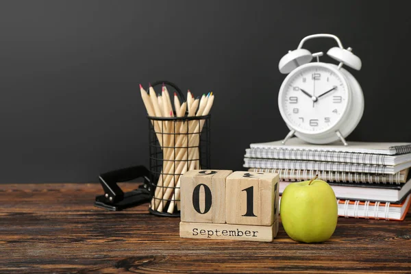 Different stationery, alarm clock and calendar with date SEPTEMBER 1 on wooden table against black chalkboard
