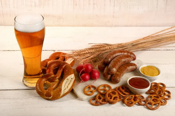 stock image Glass of cold beer and board with different snacks on light wooden background. Oktoberfest celebration