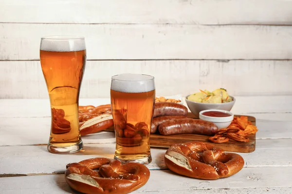 stock image Glasses of cold beer and board with different snacks on light wooden background. Oktoberfest celebration