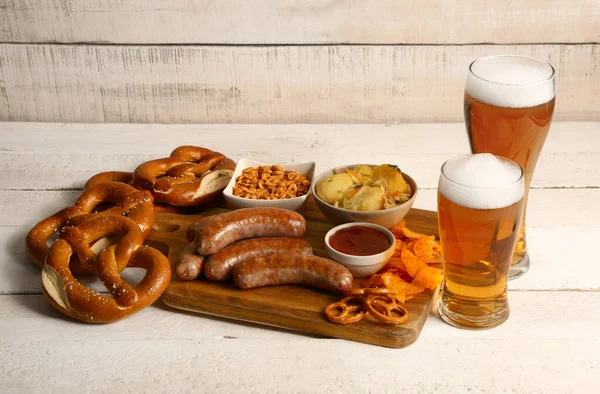 stock image Glasses of cold beer and board with different snacks on light wooden background. Oktoberfest celebration