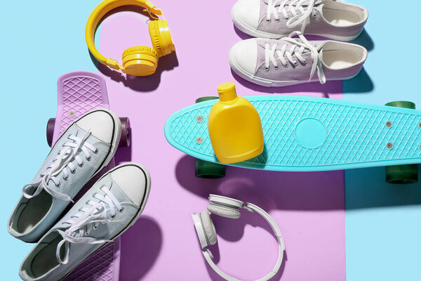 Composition with bottle of sunscreen cream, headphones, shoes and skateboards on color background
