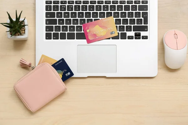 Laptop with computer mouse, wallet and credit cards on brown background