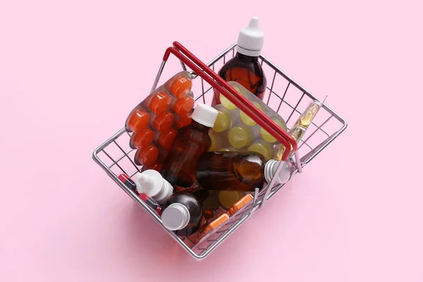 ピンクの背景に異なる薬とミニショッピングバスケット — ストック写真