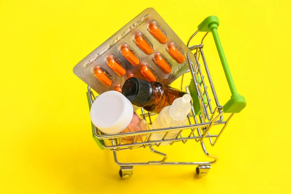 Mini shopping cart with different medicines on yellow background
