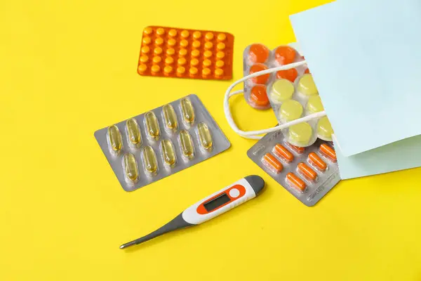 黄色の背景に異なる薬とショッピングバッグ — ストック写真