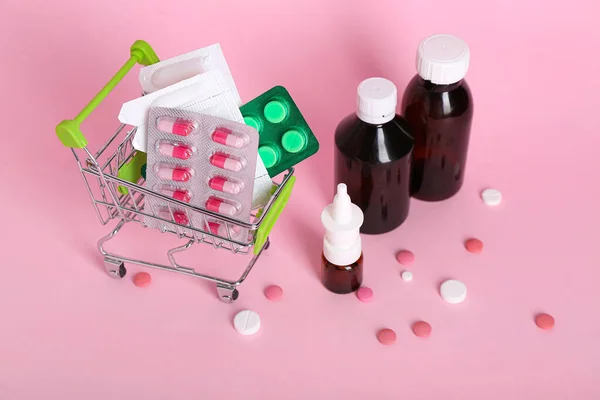 ピンクの背景に異なる薬とミニショッピングカート — ストック写真