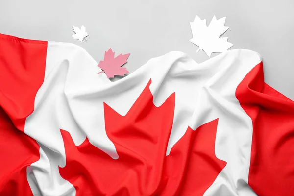 Flag of Canada and paper maple leaves on grey background