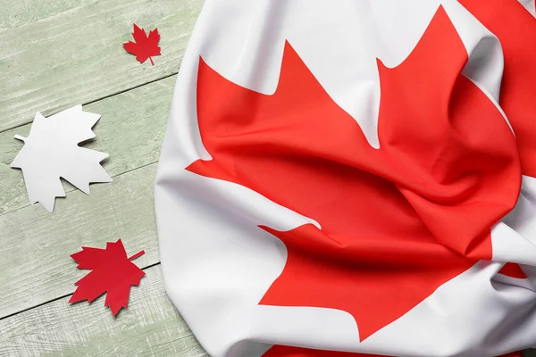 Flag of Canada and paper maple leaves on green wooden background