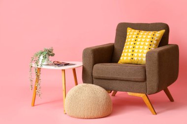 Kahverengi koltuk, pembe arka planda puf ve masa.