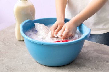 Çamaşırları gri grunge masasında plastik bir leğenle yıkayan kadın.