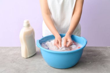 Çamaşırları gri grunge masasında plastik bir leğenle yıkayan kadın.