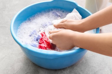 Çamaşırları gri grunge masasında plastik bir leğenle yıkayan kadın.