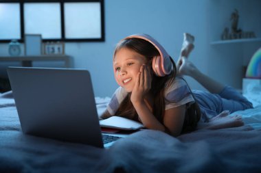 Kulaklıklı küçük kız geceleri yatak odasında internetten ders çalışıyor.