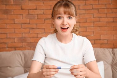 Yatak odasında hamilelik testi olan mutlu genç kadın, yakın plan.
