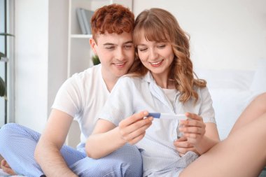 Yatak odasında hamilelik testi olan mutlu genç çift.