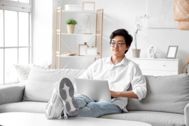 Genç Asyalı adam izin gününde dizüstü bilgisayar kullanıyor.