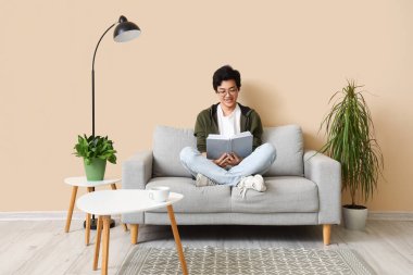 Genç Asyalı adam izin gününde evde kitap okuyor.