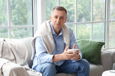 Olgun bir adam izin gününde evde çay içiyor.