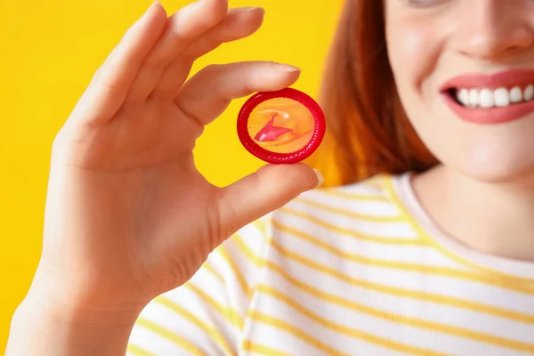 黄色の背景にコンドームを持つ若い女性 クローズアップ — ストック写真