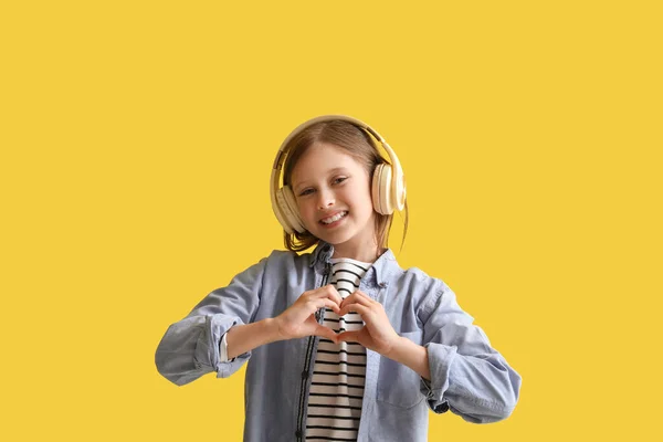 戴耳机的小女孩在黄色背景下做心形 — 图库照片