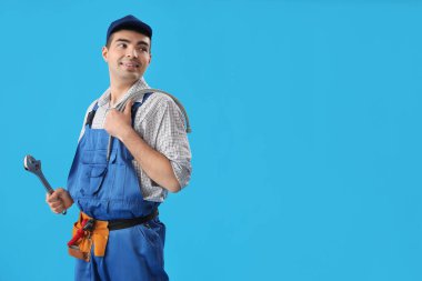 Mavi arka planda aletleri olan genç bir tesisatçı.