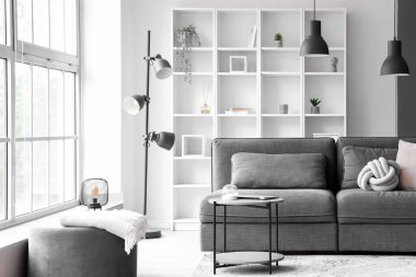 Büyük pencerenin yanında rahat gri kanepe ve sehpası olan aydınlık oturma odasının içinde.