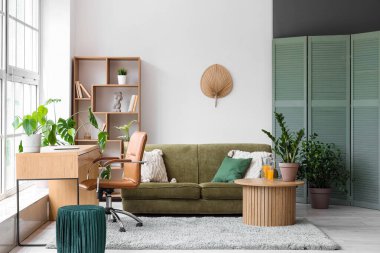 Şık, yeşil kanepeli ve büyük pencerenin yanında rahat bir çalışma odası.