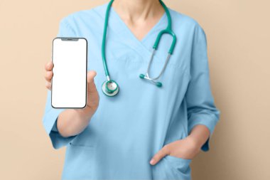 Steteskoplu kadın doktor bej arka planda cep telefonu ekranı gösteriyor.