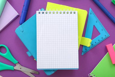 Mor zemin üzerinde farklı kırtasiye malzemesi olan boş bir defter
