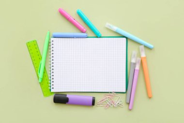 Yeşil zemin üzerinde farklı kırtasiye malzemesi olan boş bir defter