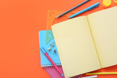 Turuncu zemin üzerinde farklı kırtasiye malzemesi olan boş bir defter
