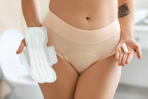 Young woman in period panties with menstrual pad and tampon at home, closeup