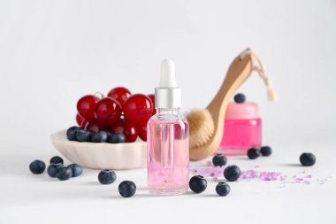 Bir şişe yağ, masaj fırçası ve beyaz arka planda taze böğürtlen.