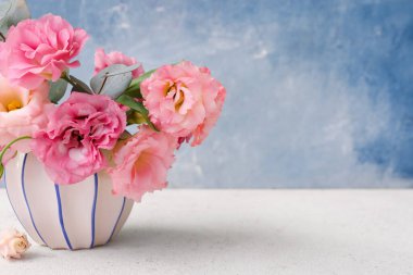 Beyaz masanın üzerinde pembe Eustoma çiçekleri olan vazo.