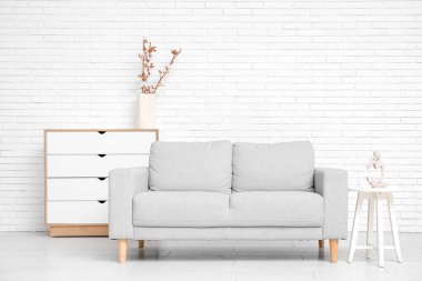 Oturma odasının içinde kanepe, çekmeceler ve beyaz tuğla duvarın yanındaki masa.