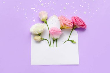 Güzel Eustoma çiçekleri ve mor arkaplanda konfeti olan boş bir zarf.