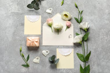 Boş kartlı kompozisyon, nişan yüzüğü, zarf ve gri arka planda güzel Eustoma çiçekleri.