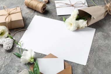 Gri arkaplanda boş kart, zarf, iplik ve güzel Eustoma çiçekleri olan kompozisyon, yakın plan.