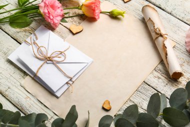 Boş kartlı kompozisyon, zarflar, okaliptüs dalı ve hafif ahşap arka planda güzel Eustoma çiçekleri, yakın plan.