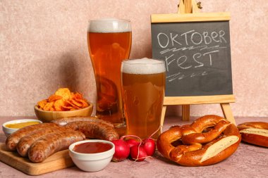 Soğuk bira bardakları, kelime karatahta OKTOBERFEST ve pembe arka planda farklı atıştırmalıklar